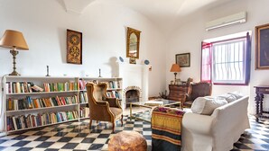 Een woonkamer met een zwart-witte vloer, een open haard, een boekenplank, een bank en een lamp.