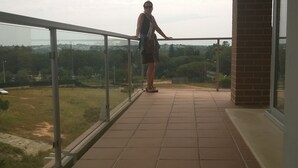 Un balcon doté d’une balustrade en verre, donnant sur une pelouse et un pont situé au loin.