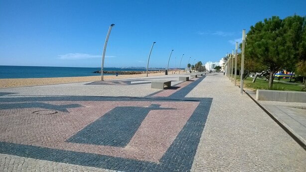 Une promenade dallée avec des flèches indiquant le sens, une plage et des lampadaires.