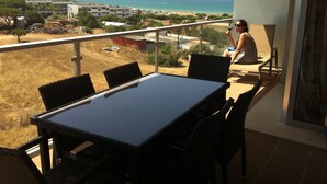 Un balcon doté d’une balustrade en verre, offrant une vue sur une plage et des bâtiments.