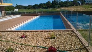 Une piscine rectangulaire à l’eau d’un bleu limpide, entourée d’une terrasse bordée de galets et d’une clôture en métal.
