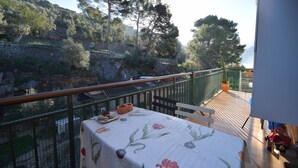 A balcony with a table set for dining, overlooking a rocky hillside with trees and a building in the distance. - Brasilia 5A - Apartment in Puerto de Sóller with views to the sea and  mountains (Puerto de Sóller)