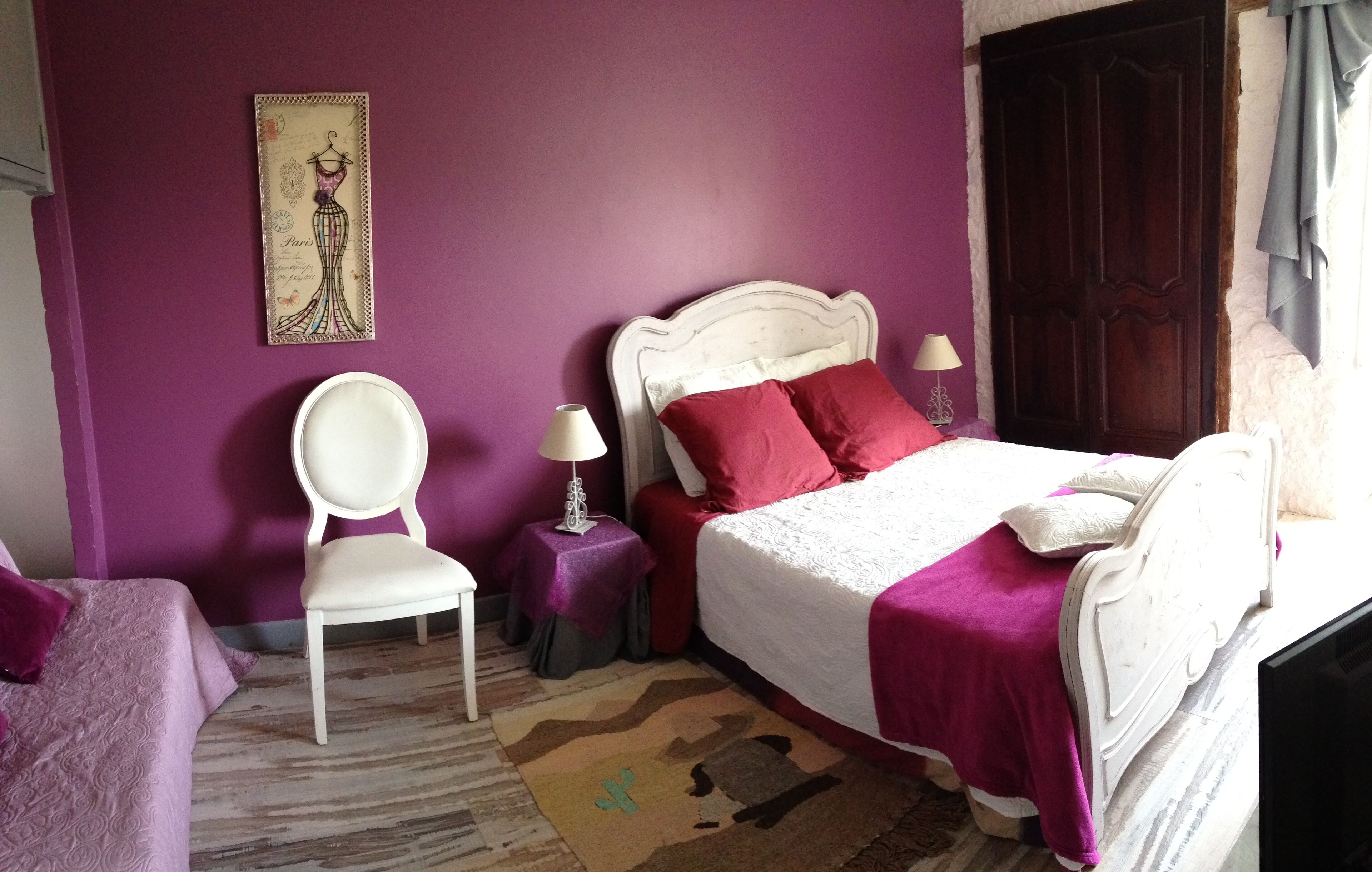 Un dormitorio con una cama, una silla, una mesita de noche y un cuadro colgado en la pared.