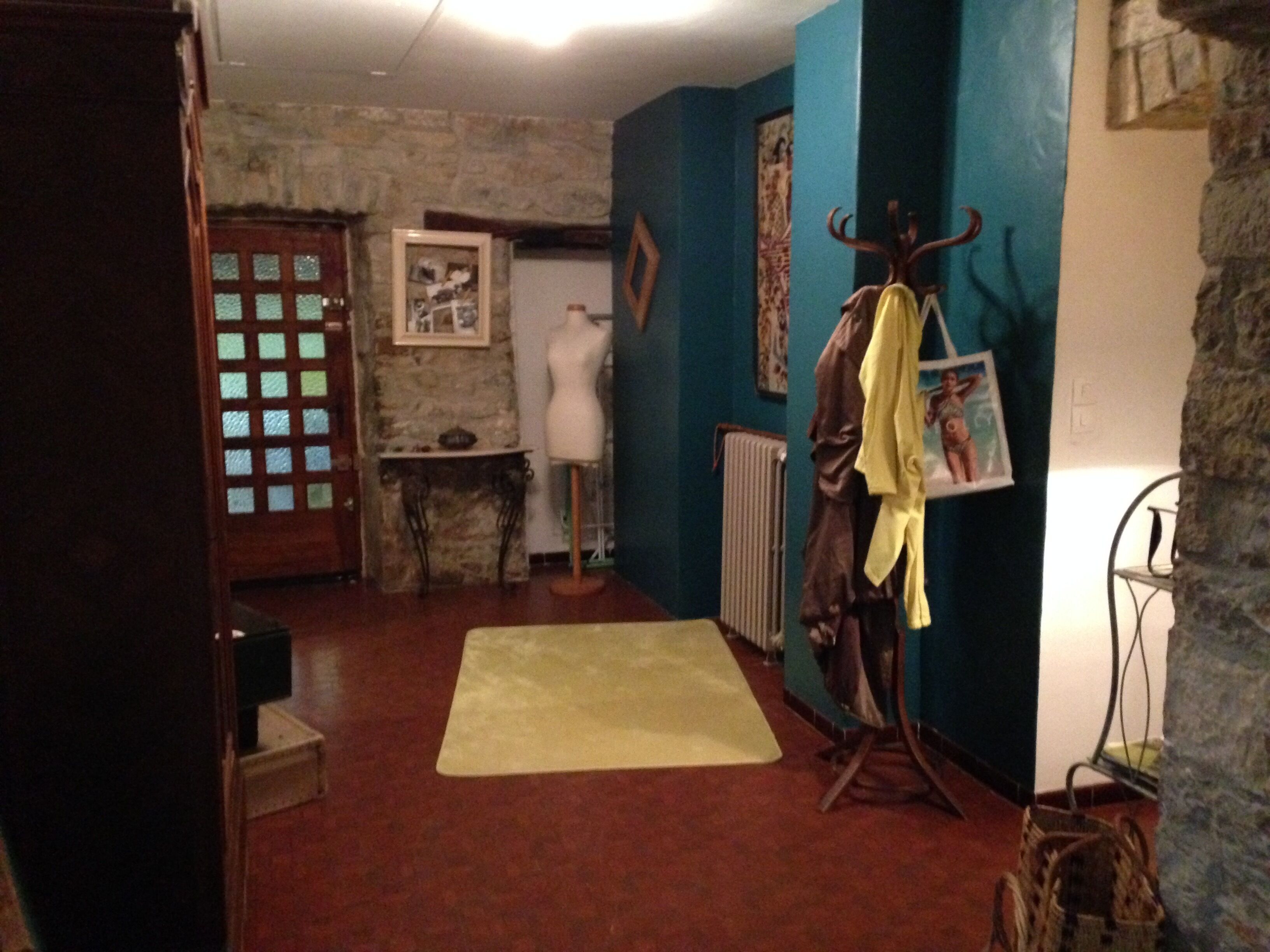 Een kamer met een stenen muur, een etalagepop in een geel kledingstuk, en een lijst met een afbeelding aan de muur.