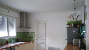 Een compacte keuken met een houten aanrecht, een ingebouwde vaatwasser, een spoelbak en een kookplaat. Er staan twee stoelen bij een kleine tafel, en een deur met een groene omlijsting.