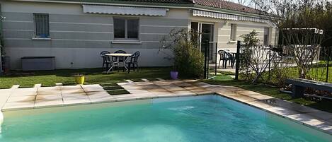 A residential property with a swimming pool, a patio with outdoor furniture, and a well-maintained lawn.
