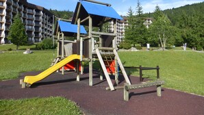 Un'area giochi con uno scivolo e strutture per arrampicarsi, circondata da un prato e un edificio residenziale sullo sfondo.