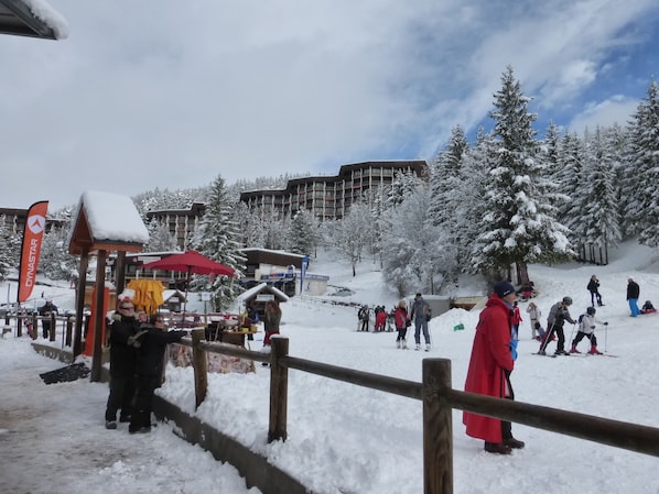 A snowy outdoor area with a wooden fence, a red umbrella, and people skiing.