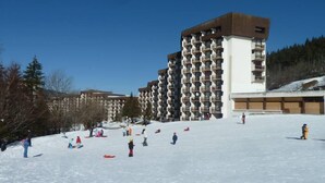 Una stazione sciistica con diversi edifici alti, probabilmente parte di un complesso alberghiero, con balconi e cielo sereno.