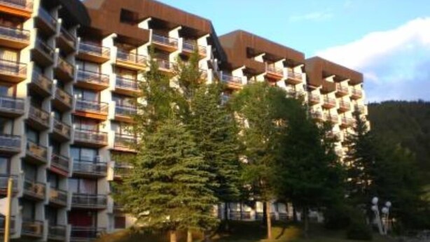 Un hotel a pi ù piani con balconi, immerso nel verde e sotto un cielo sereno.