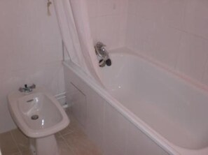 Ein Badezimmer mit einer Badewanne, einem kleinen Waschbecken und einem Spiegel.
