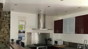 A modern kitchen with a central island, dark cabinetry, a stainless steel range hood, and a stone accent wall. - Groix: Authentic fisherman's house close to any convenience (Groix)