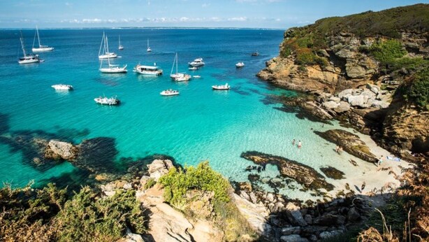 A coastal area with clear turquoise waters, rocky cliffs, and boats anchored in the bay. - Groix: Authentic fisherman's house close to any convenience (Groix)