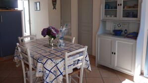 A dining area with a table set for four, surrounded by chairs, a cabinet with kitchenware, and a television on a stand. - house / villa - LA GUERINIERE (La Guérinière)