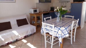 A cozy living area with a white sofa, a dining table with chairs, a kitchen area with a microwave, and a TV. - house / villa - LA GUERINIERE (La Guérinière)