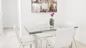 Ein moderner Essbereich mit einem Glastisch, weißen Stühlen und einem Stadtbild an der Wand.