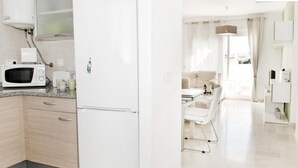 Eine moderne Küche mit Mikrowelle, Toaster und Kühlschrank. Es gibt einen Essbereich mit Tisch und Stühlen sowie einen Blick ins Freie durch große Fenster.