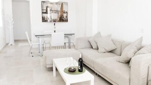 Ein modernes Wohnzimmer mit einem beigen Sofa, einem weißen Couchtisch und einem Essbereich mit einem Glastisch und Stühlen.