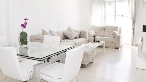 Ein modernes Wohnzimmer mit einem Glastisch, weißen Sofas und einem Couchtisch aus Glas.