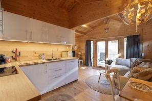 Cozy cabin with a well-appointed kitchen, comfortable sofa set, and dining table, surrounded by wooden beams.