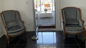 Una habitación con dos sillones decorados, una puerta de cristal que da a un balcón y un suelo de baldosas.