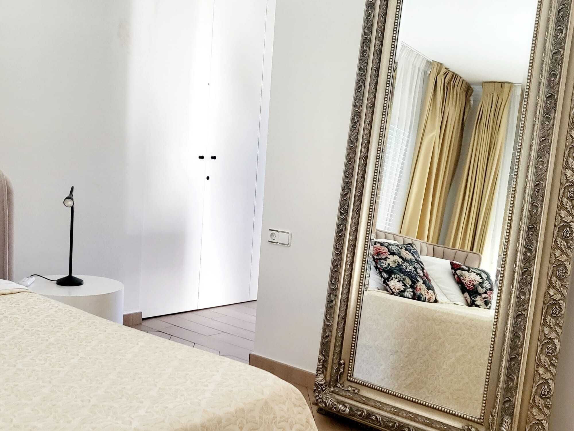 Une chambre à coucher avec un grand miroir décoratif, une lampe de chevet et un lit agrémenté d’un coussin à motifs floraux.