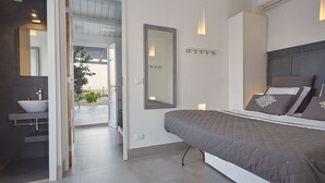 Quarto moderno com uma cama grande, luminárias de cabeceira, espelho e banheiro com pia e chuveiro.