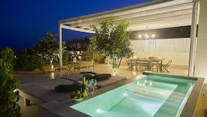 Uma área de piscina ao ar livre com pérgula, assentos e mesa de jantar.