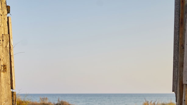 Uma trilha de areia que leva ao oceano, ladeada por estruturas de madeira e vegetação.