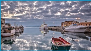 Um porto com barcos atracados, um navio grande ao centro e edifícios ao longo da orla.