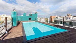Una piscina al terrat amb un pont de fusta, envoltada de parets amb rajoles turquesa i un cel blau clar.