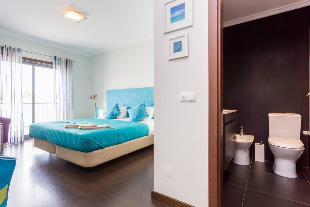 A bedroom with a bed, a bathroom with a toilet and bidet, and a view of the outdoors.