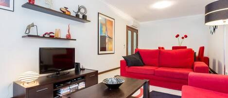 A modern living room with a red sofa, a flat-screen TV, and a coffee table.