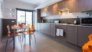 Cuina moderna amb armaris grisos, fogó a gas i microones. Hi ha una zona de dinar amb cadires taronja i una taula.