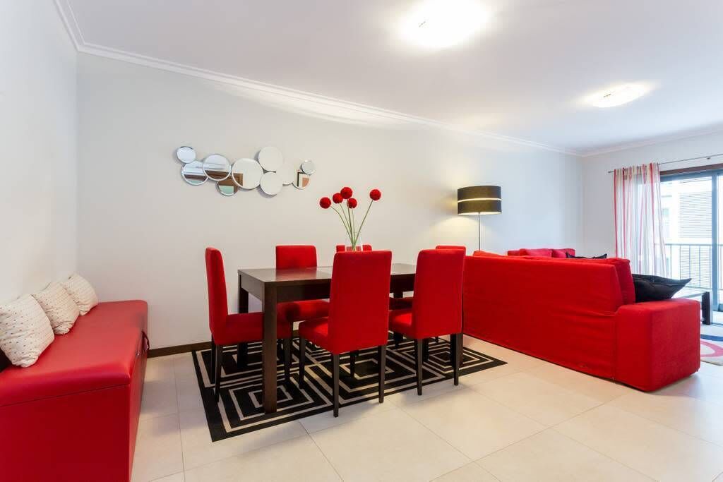 A modern living room with a red sofa, a dining table with red chairs, and a black and white patterned rug.