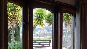 Habitación con tres ventanas que dan a un jardín y una vista distante de edificios.