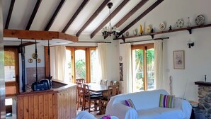 Un amplio salón con techo alto, vigas de madera, una mesa de comedor y dos sofás blancos.
