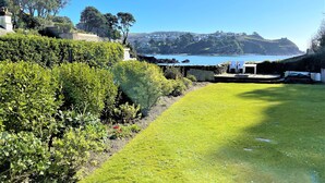 A coastal garden with a lawn, a white gazebo, and a view of the sea and distant hills. - Seaweed Cottage in Fowey overlooking the beach with a garden and a parking space (Fowey)
