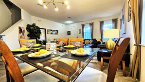 Uma sala de jantar com mesa de vidro posta para quatro pessoas, cadeiras de madeira e um sofá ao fundo.