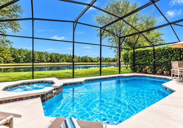 A swimming pool with a hot tub, surrounded by a covered area with a view of a lake and trees.