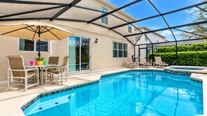 A swimming pool with lounge chairs and a table, surrounded by a covered patio area.
