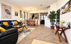 A modern living room with a black leather sofa, wooden dining table, and a large potted plant.
