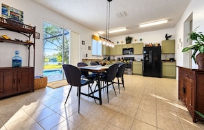A modern kitchen with a dining area, large windows, and a view of a swimming pool.