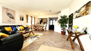 Uma sala de estar moderna com um sofá de couro preto, mesa de centro de madeira e um espaço de jantar com cadeiras de madeira e mesa de vidro.