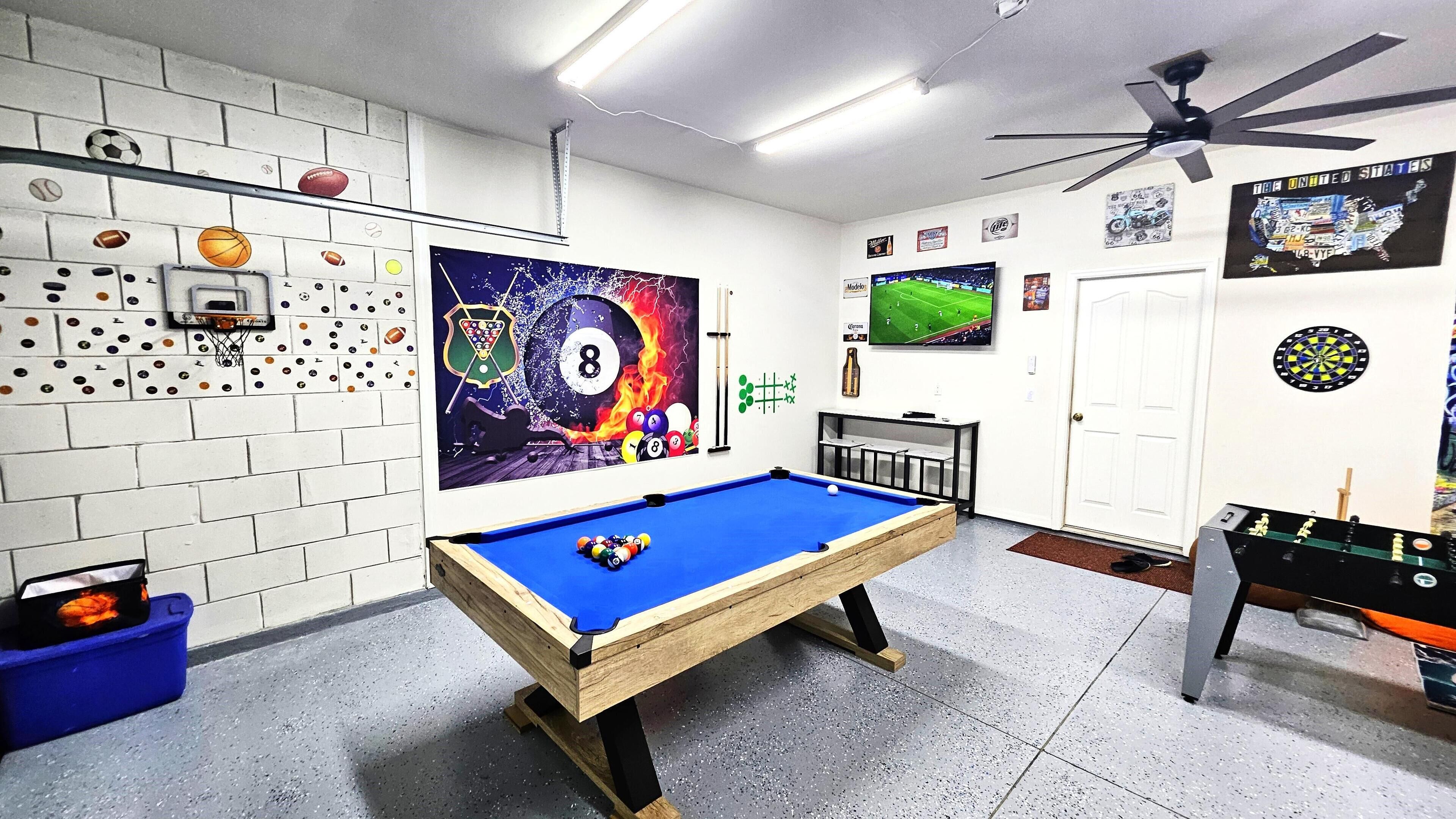 A pool table in a room with a dartboard, a foosball table, and various sports memorabilia on the walls.