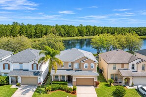 A row of single-family homes with attached garages, surrounded by lush greenery and a lake. - BlueLakeView Villa – Private Pool & Spa, Stunning Lake Views, BBQ & Games Room (Clermont)