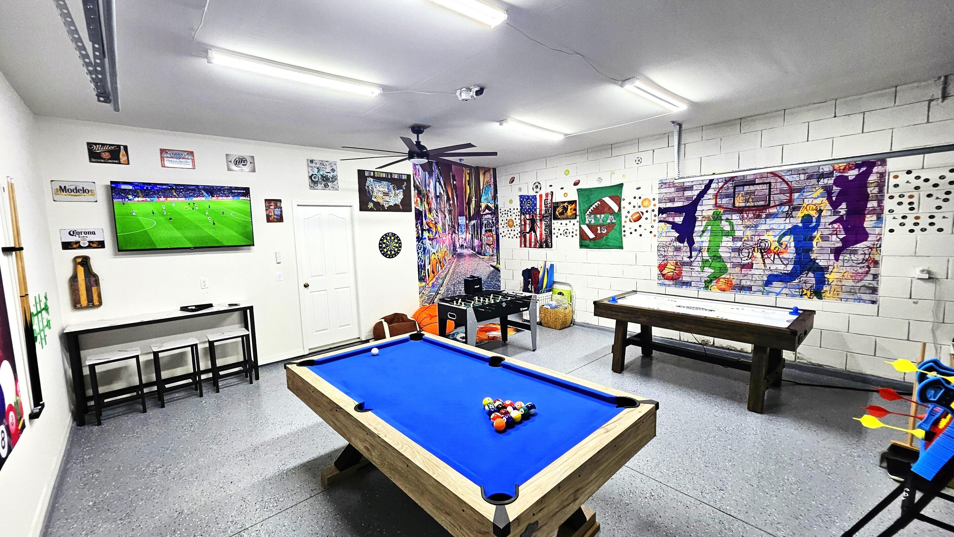 Een recreatieruimte met een pooltafel, tafelvoetbal, dartbord en een televisietoestel waarop een voetbalwedstrijd wordt vertoond.