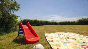 A grassy field with a red slide, a soccer ball, and a colorful blanket. - Scandinavian Cabin near Bude with Log Burner (Kilkhampton)