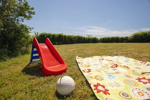 Un campo cubierto de césped con un tobogán rojo, una pelota de fútbol y una manta colorida.