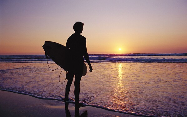 A silhouette of a person carrying a surfboard on a beach at sunset. - Scandinavian Cabin near Bude with Log Burner (Kilkhampton)